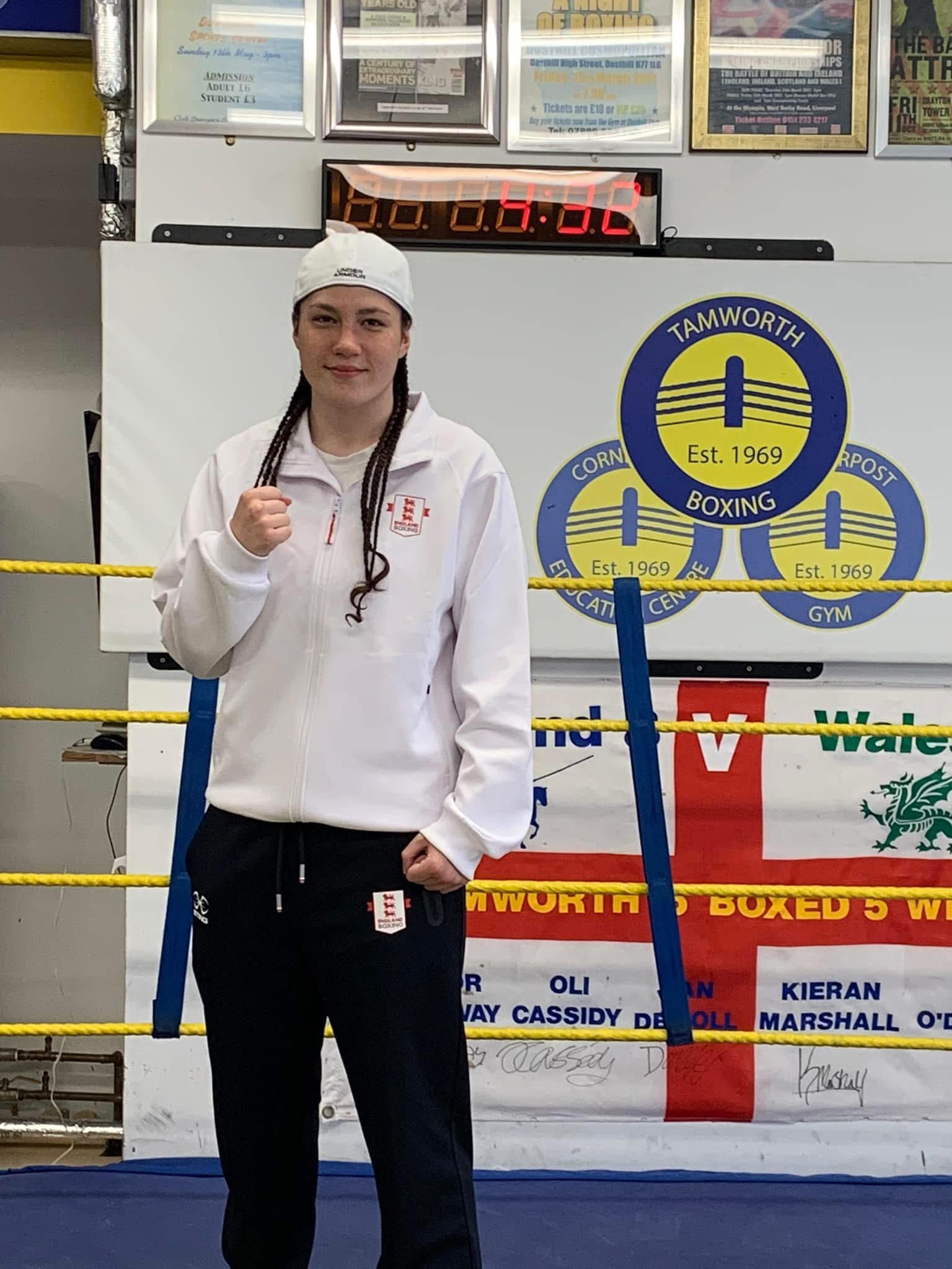 An England boxer in national kit in front of the Tamworth Boxing crest in the gym