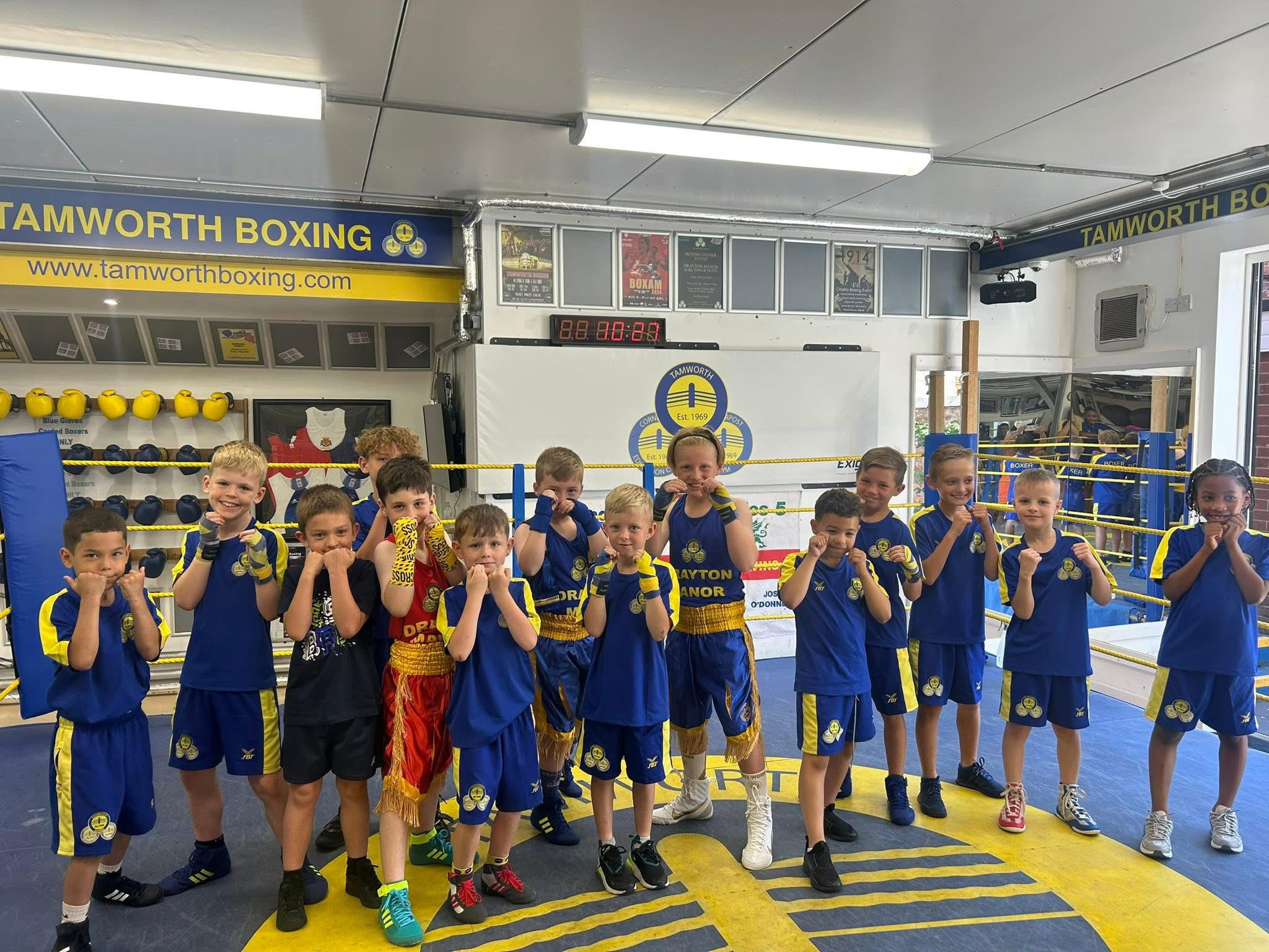 The minors group lined up in club kit on the gym floor, fists up
